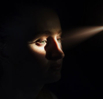 A person's face in the dark, with light shining in from a small opening.
